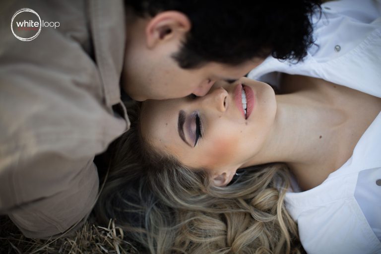 The groom kissing the bride on the forehead lying on grass, enjoying the moment with eyes closed