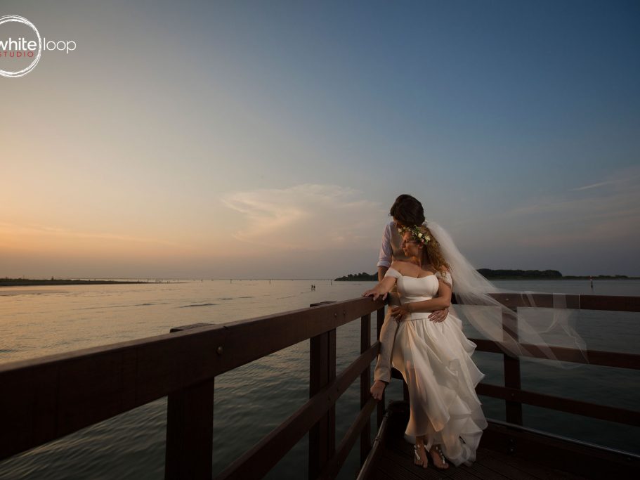 The bride and groom holding each other on a dock watching the sunset on the horizon of the sea.