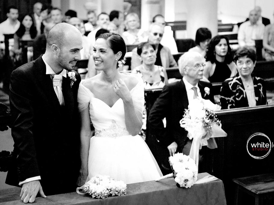 The bride talking with groom in the middle of the ceremony in the church, while mum is tenderly watching, projecting the picture in black and white as a symbol of elegance and finesse of the moment.
