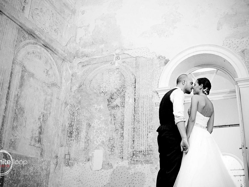 The bride and groom are kissing in black and white in an ancient room with frescos in the historical Italian environment.